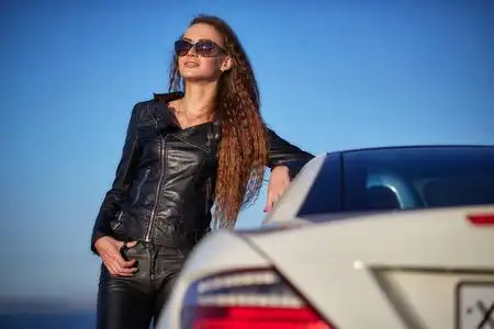 美丽性感的女孩,长头发在一件皮夹克,太阳镜的皮裤下车在日落时分照片