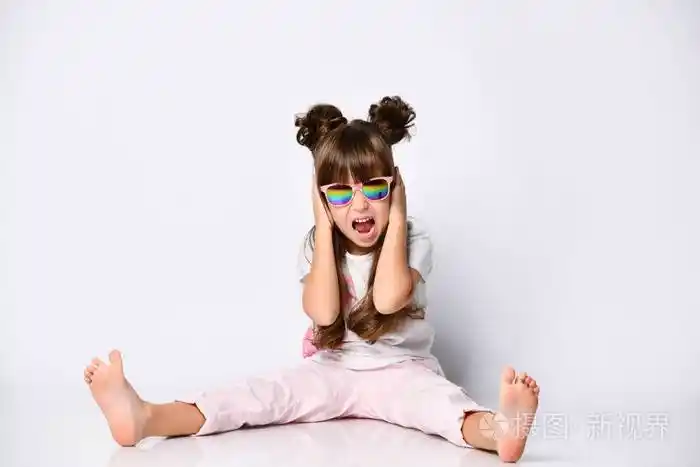 女孩的姿势坐在地板上在工作室戴着太阳镜和时尚的发型赤脚