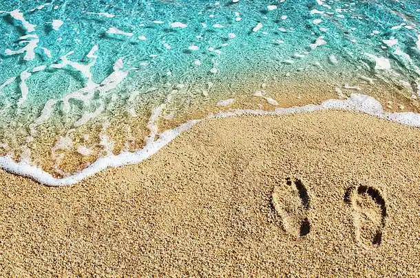 黄沙上的两个脚印蓝色的海浪白色泡沫顶视图