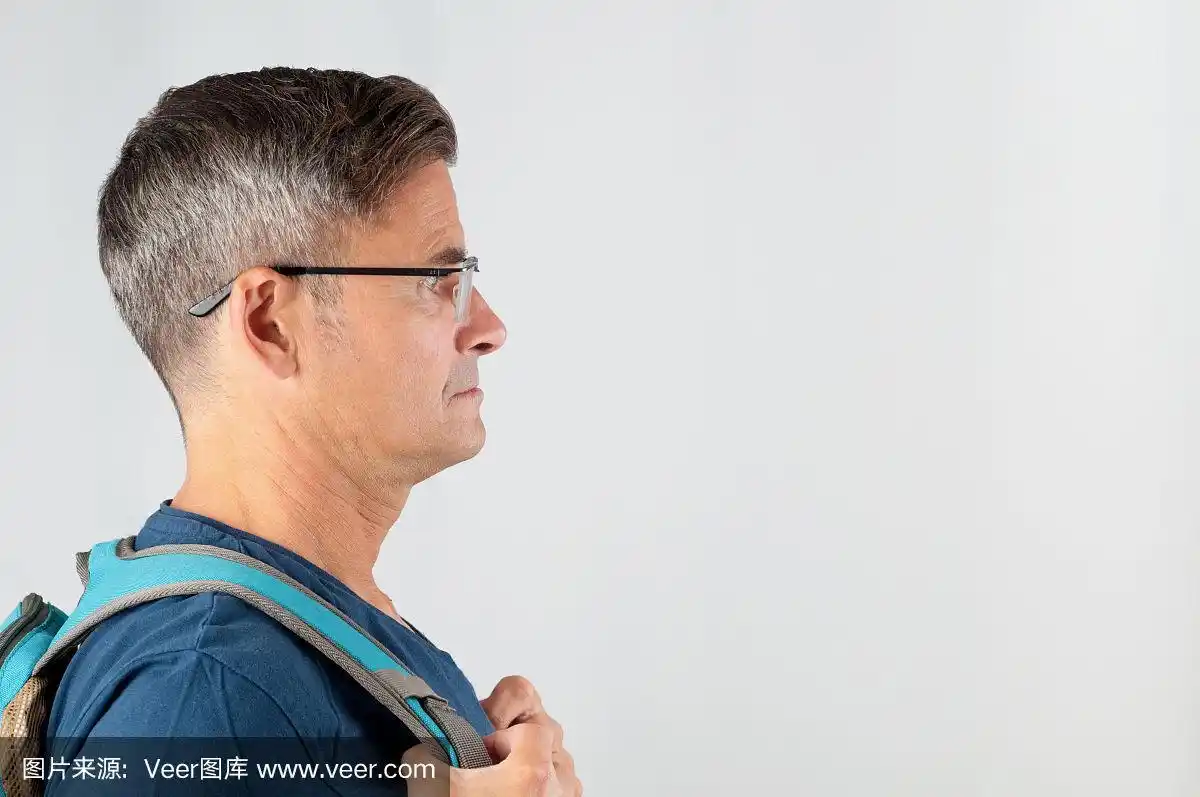 在灰色背景上戴眼镜和背包的资深男子的侧视图