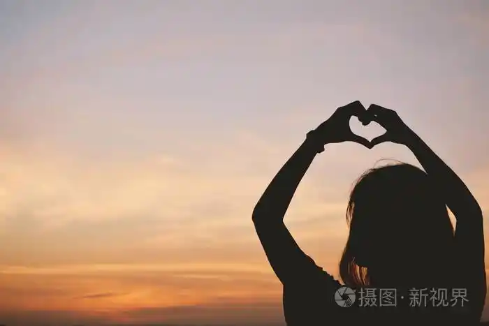 妇女在天空日落背景心形的剪影手