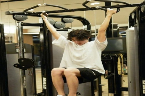 照片中,王俊凯身穿白色宽松t恤和黑色短裤,正在做引体向上动作.