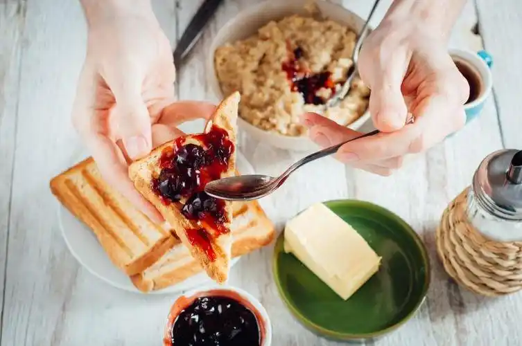 木桌上正在沾着果酱吃烤面包的男士