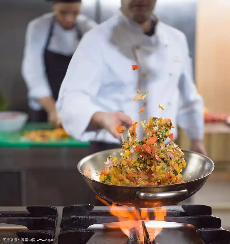 年轻男厨师在商业厨房炒菜.厨师在锅里翻炒蔬菜