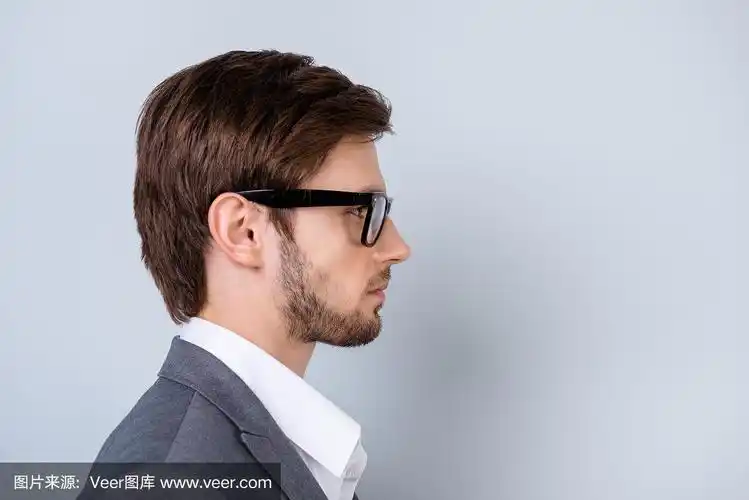 侧视图特写的年轻成功的严肃的男人戴着眼镜站在灰色的背景