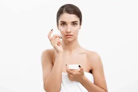 美容青年护肤概念-关闭美丽的白种女人脸肖像涂抹一些奶油她的脸.