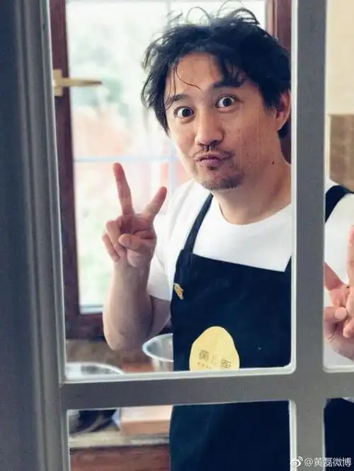 "照片中,黄磊系着围裙,乱而有点长的头发,瞪着圆眼嘟嘴比v卖萌,尽显