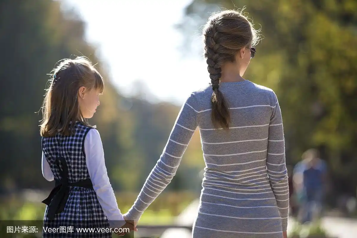 在温暖的日子里,孩子女孩和母亲在一起手牵手的衣服的背影