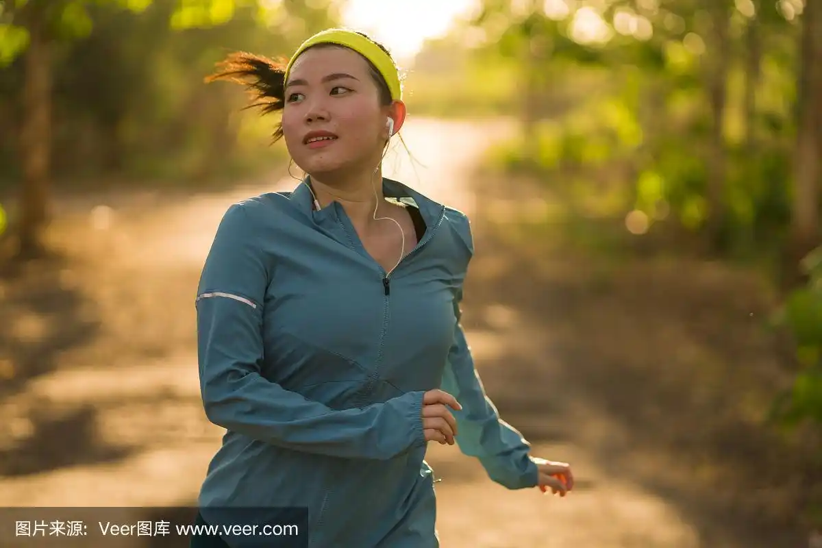 迷人而健康的中国女孩在美丽的乡村道路上慢跑,以树木为背景,以跑步者
