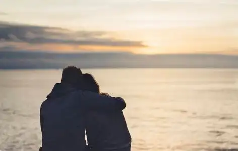 海洋上的日出夫妇在背景海洋日出在沙滩上拥抱,两个浪漫的人的侧影