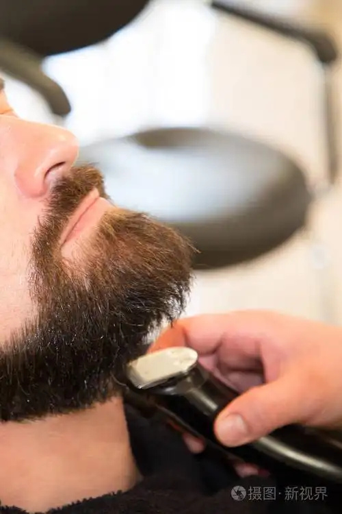 理发店里坐着的一个留着胡子的年轻人,由专业理发师修剪胡须