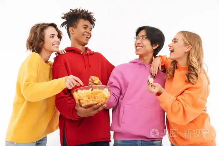 中年轻的一群朋友,学生孤立地站在白色的墙壁背景上,互相交谈,吃薯片