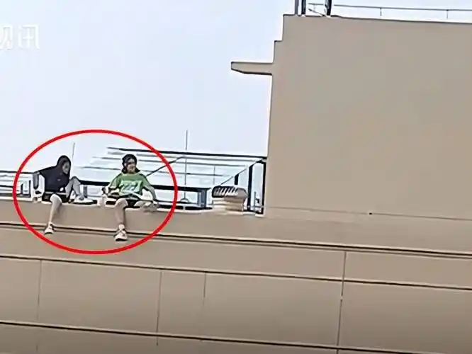 两个女孩坐在28层楼楼顶边缘的女儿墙上玩耍:无知无畏_男子_胆子_双脚