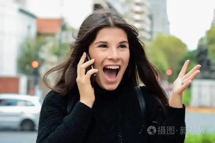 一个惊讶的女人在智能手机上说话时张开嘴的肖像户外城市城市背景