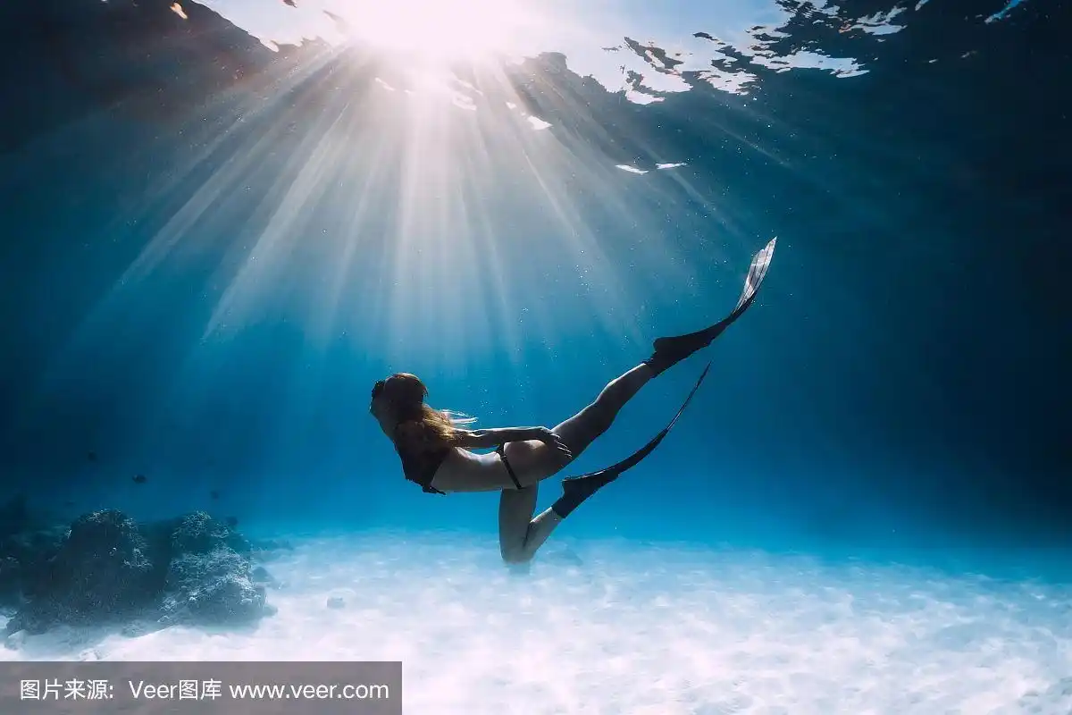 年轻女子自由潜水者滑过沙海与鳍.
