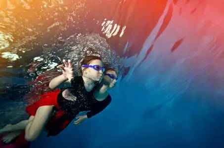 游泳在水之下两个漂亮的小女孩一起游泳水下对明亮的灯光,穿着红色的