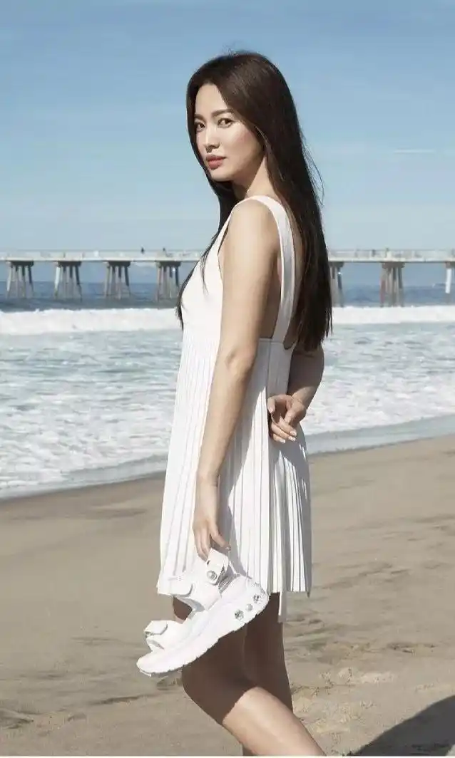 宋慧乔全新美照曝光,吊带露脐装显丰满,穿白裙拎着鞋在沙滩漫步