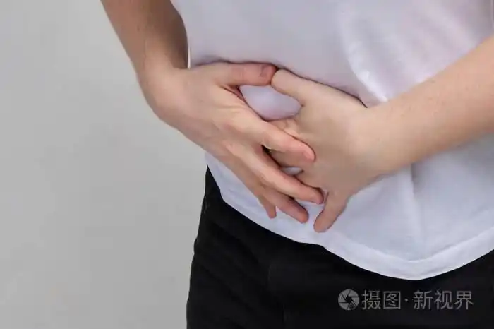 一个穿白t恤的男人疼得紧紧抓住肚子.食物中毒概念.