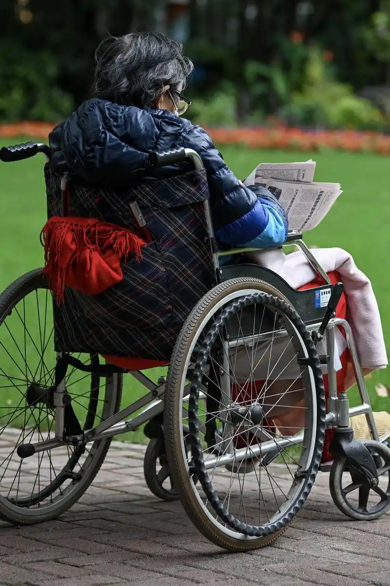 2021年10月18日,上海襄阳公园,一位身穿羽绒服的老人坐在轮椅上看报纸