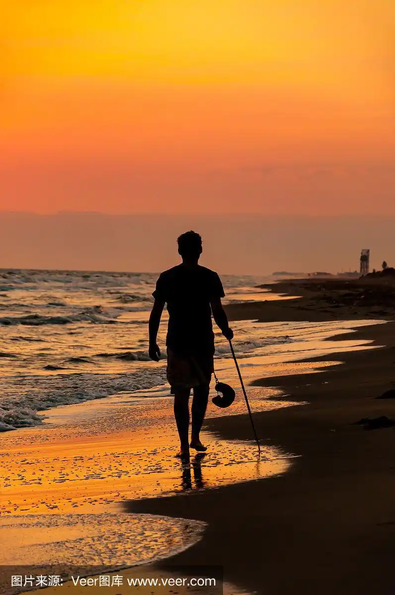 那个戴着帽子和手杖在日落时分走在海滩上的男人.彩色的背景.