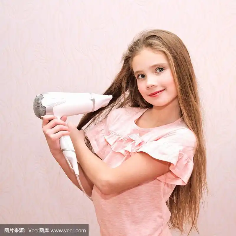 可爱的微笑小女孩用吹风机吹她的长发
