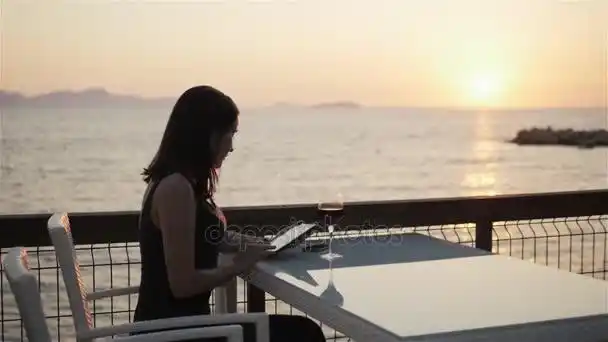 年轻的黑发女郎杯红酒坐在海边的.