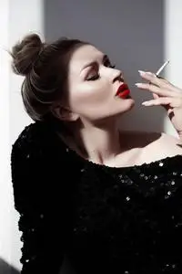 一个美丽的年轻女人谁吐出烟雾的时尚肖像照片