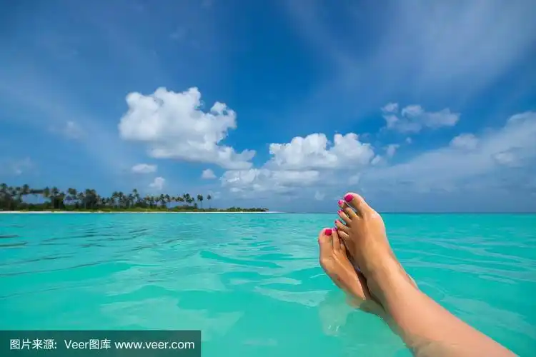 在热带海滩上的蓝色海水中的女性脚的特写.假期假期.