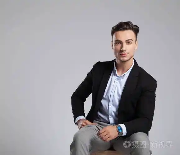 穿着黑色西装坐在浅灰色背景的木椅上的迷人商人肖像