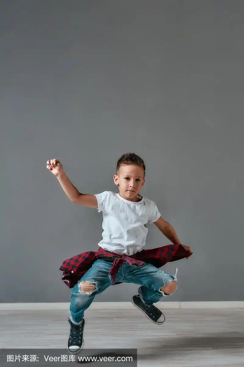 活跃的孩子.全身像兴奋的小男孩在休闲衣服跳和看着相机在工作室