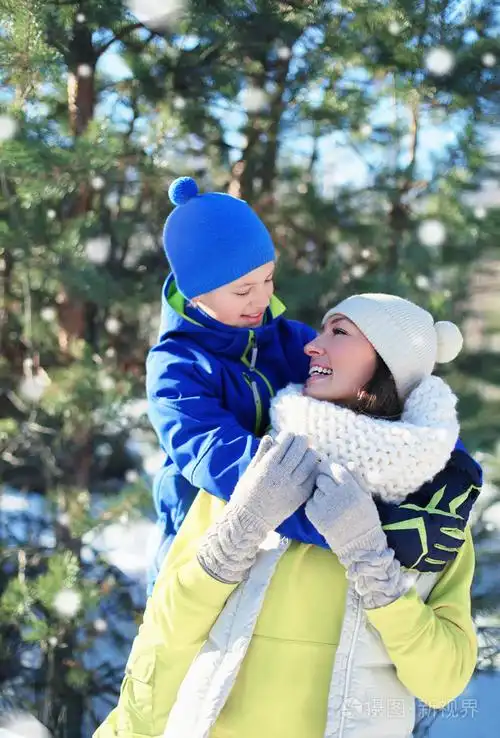 孩子抱着他的妈妈和在冬天,阳光明媚的雪在一起玩得开心