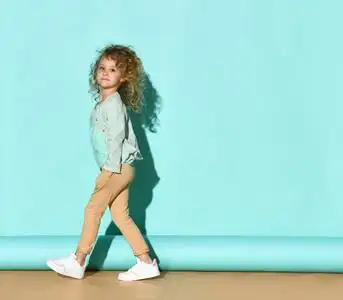 她微笑着,双手插在口袋里,在绿松石背景上侧身摆姿势照片