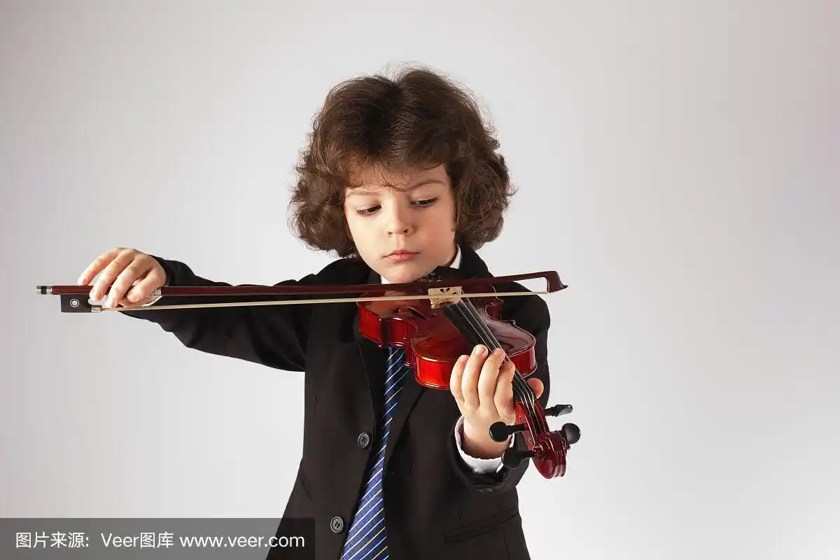 漂亮可爱的小男孩在拉小提琴.灰色的背景.