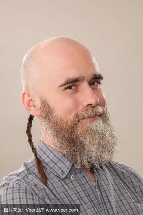 一名40岁剃着光头的大胡子男子的工作室肖像,他穿着一件米色背景的