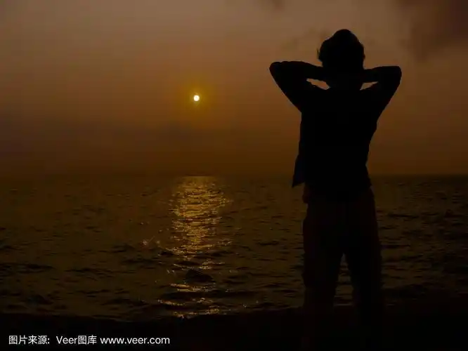 背影剪影的男人放松在日落在海上.成功的概念.