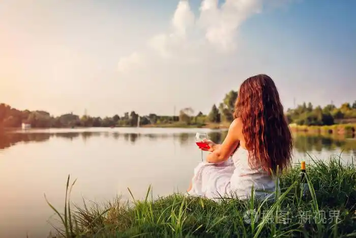 夕阳西下一位年轻女子在河边喝着葡萄酒喝酒欣赏风景的女人