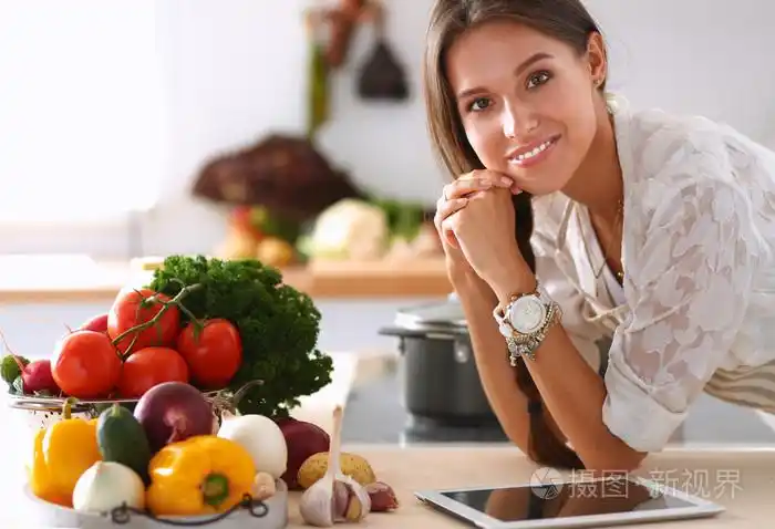 使用一台平板电脑,在她的厨房里做饭的年轻女人