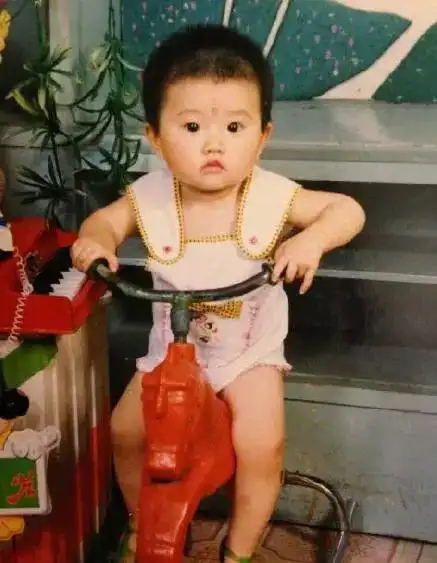 照片中,小时候的景甜骑在一辆儿童自行车上,眉毛之间也要点眉心一点红