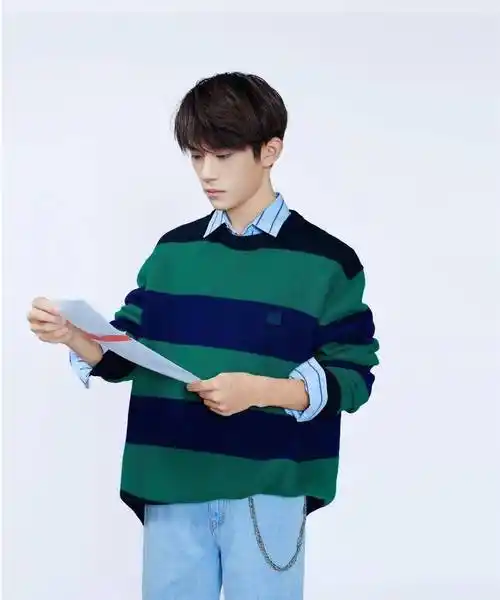 易烊千玺身穿蓝绿条纹撞色毛衣,内搭浅蓝衬衫,下身搭配浅色牛仔裤