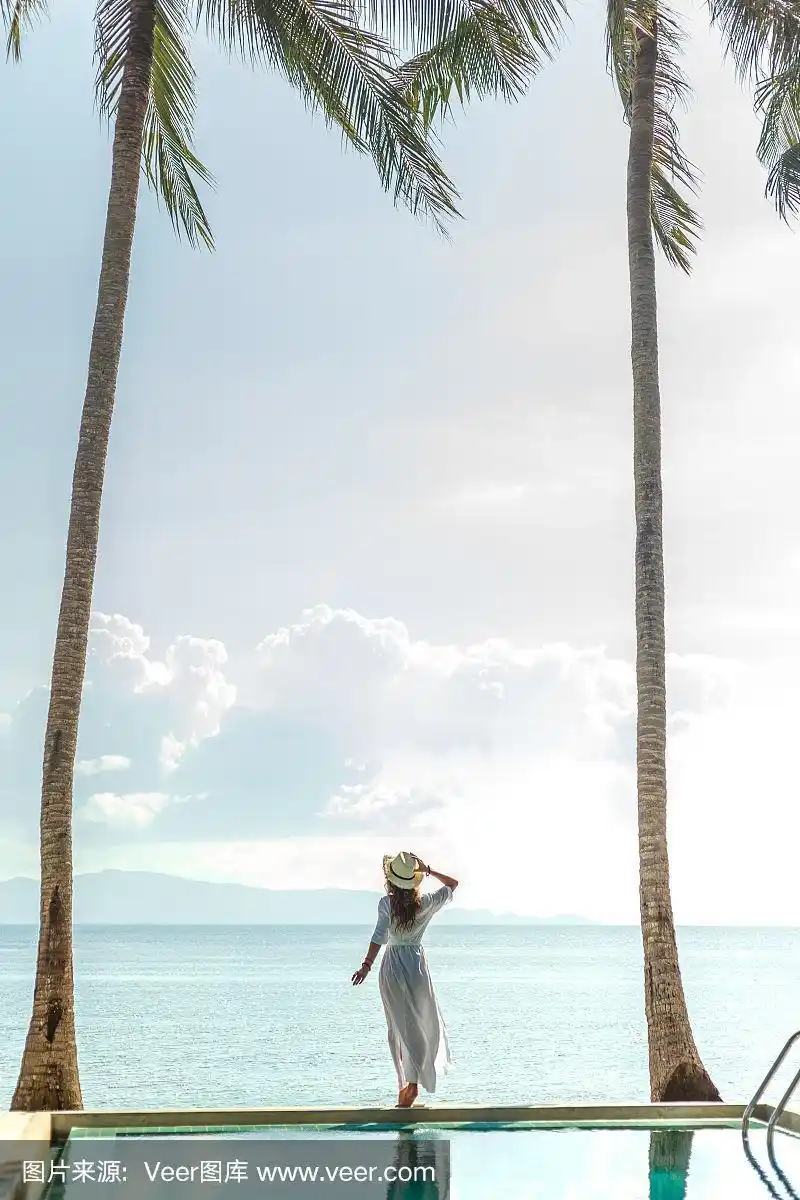 背影女孩站在游泳池与两个手掌和看海洋