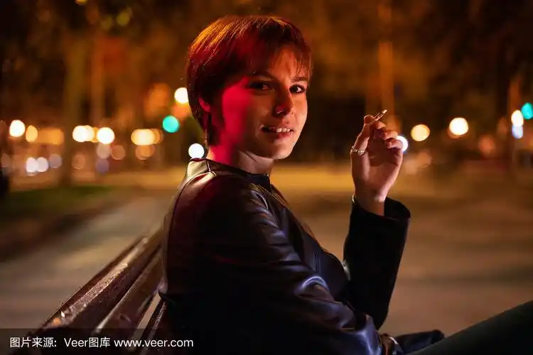一名年轻女子晚上在街道的一张木凳上抽烟