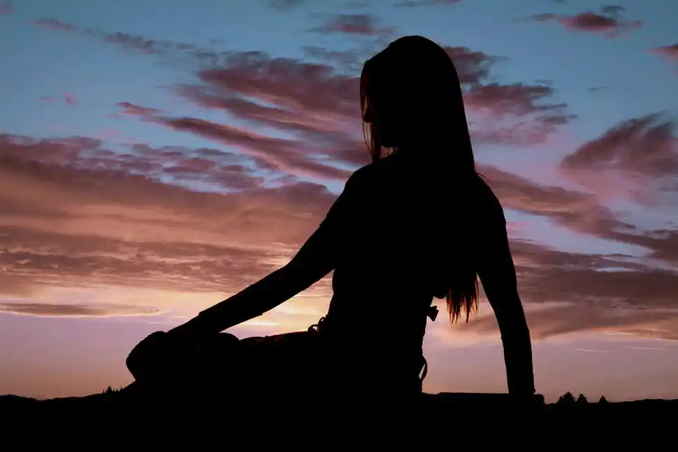 剪影夕阳女孩,一个女人坐在和坚持她的帽子往下看