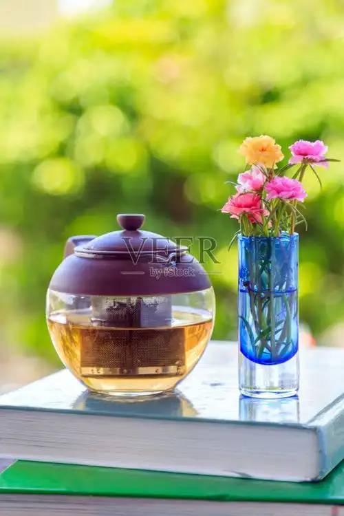一个茶壶和鲜花插在花瓶里的一本书与自然背景.