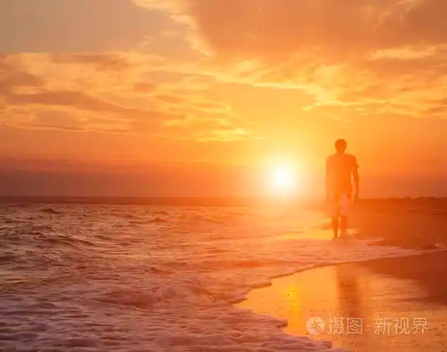 一个年轻男子在海滩上散步的剪影在一个美丽的日落的背景下