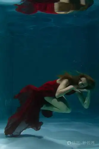 一个美丽的自由潜水员,一个人穿着红色的长裙,独自在深水中游泳