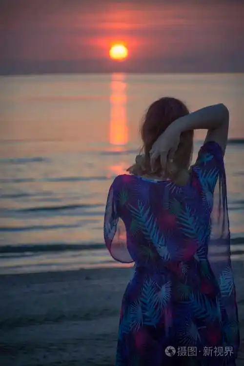 一个女人站在海滩上看着大海里的日出