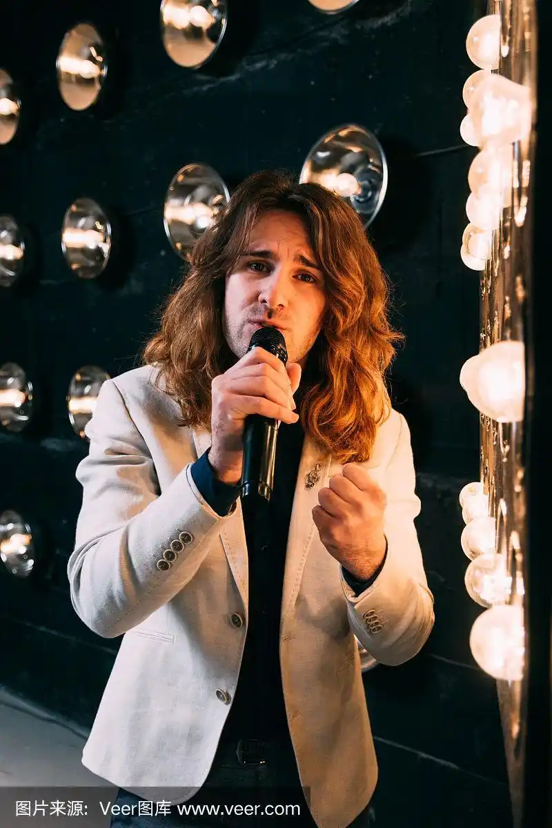 男歌手留着长发,拿着麦克风站在舞台上