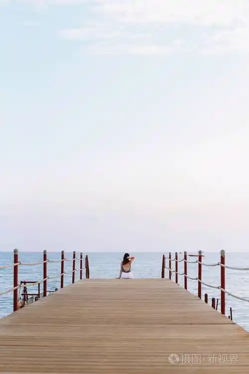 女孩坐在码头上看着海的地平线和蓝天在海上度假夏季时间海洋度假背景