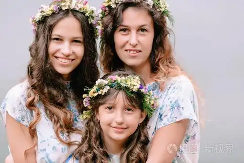 妈妈和两个女儿穿着白色裙子着花环的野花在湖边散步