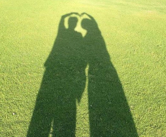 窦骁与一位女子在绿茵上并肩而立,温暖的阳光下,二人合力比出一个心形